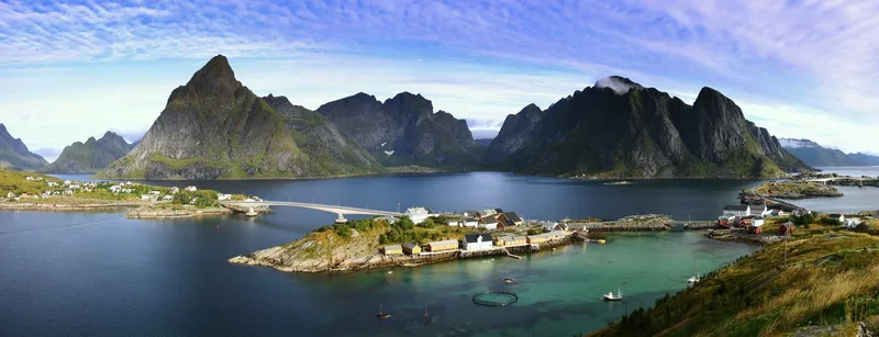 Panoramablick auf die Lofoten in Norwegen mit dramatischen Bergen, Fjord und kleinem Fischerdorf.