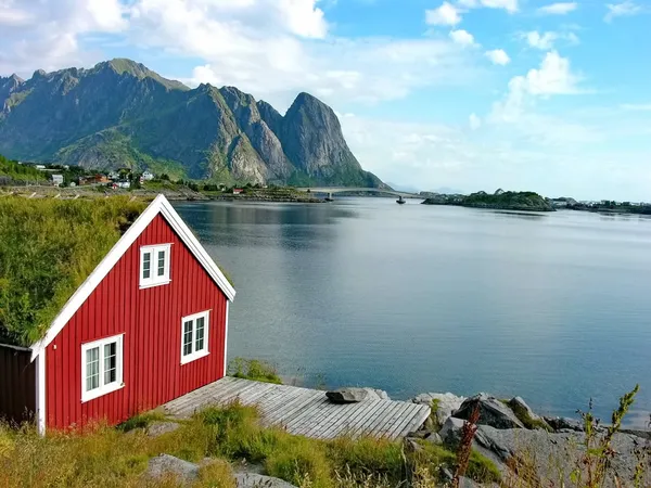 Rotes Fischerhaus an einem ruhigen Fjord auf den Lofoten mit beeindruckenden Bergen im Hintergrund.