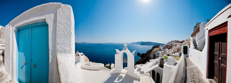 Malerische Gasse in Oia auf Santorin mit weißen Häusern, blauer Tür und Blick auf die Ägäis.